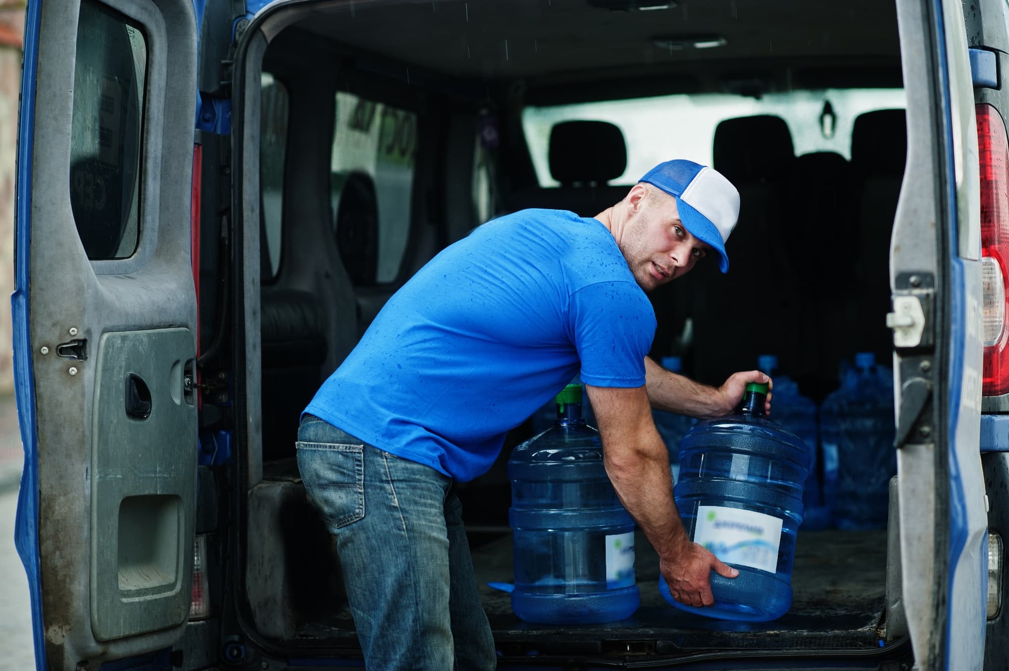 Delivery man in front cargo van delivering bottles of water.