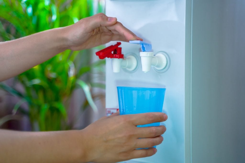 Office Water Dispenser.Woman hand serving water of a water cooler in plastic cup